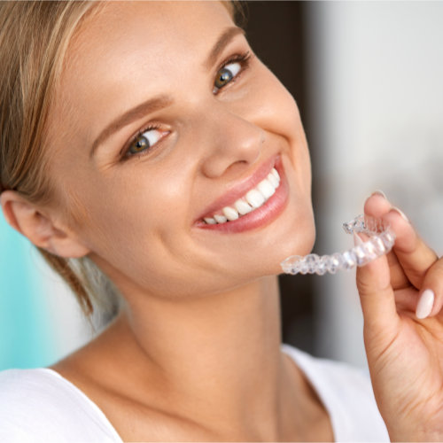 Women holding clear aligners in her hand and smiling.